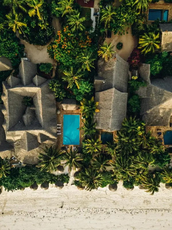 Vue aérienne d'un complexe hôtelier tropical avec des toits de chaume et une piscine.