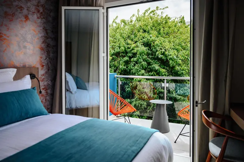 Une chambre lumineuse s'ouvre sur un balcon verdoyant.