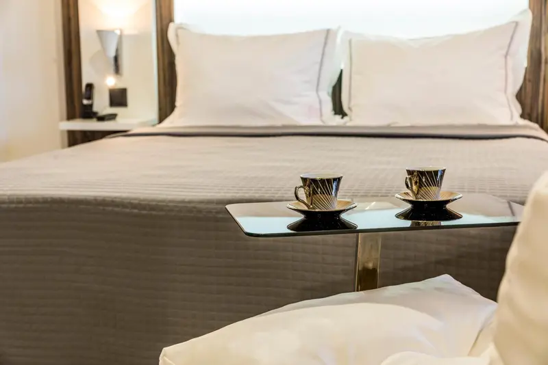 Un lit préparé avec deux tasses à café sur une petite table.