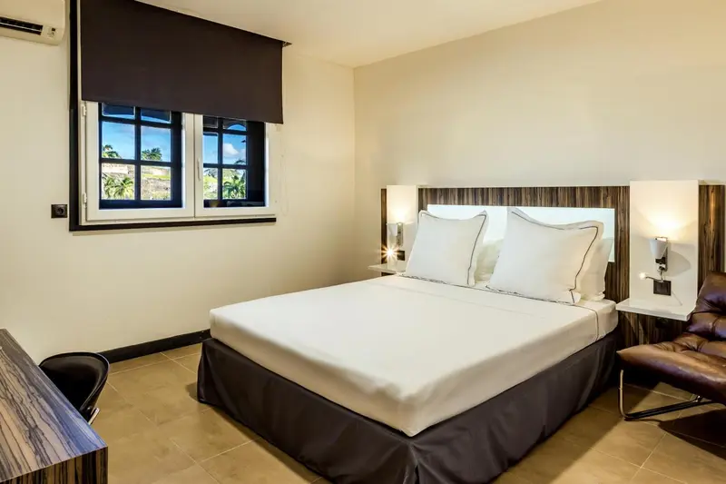 Une chambre lumineuse avec un grand lit blanc et une vue sur la végétation.