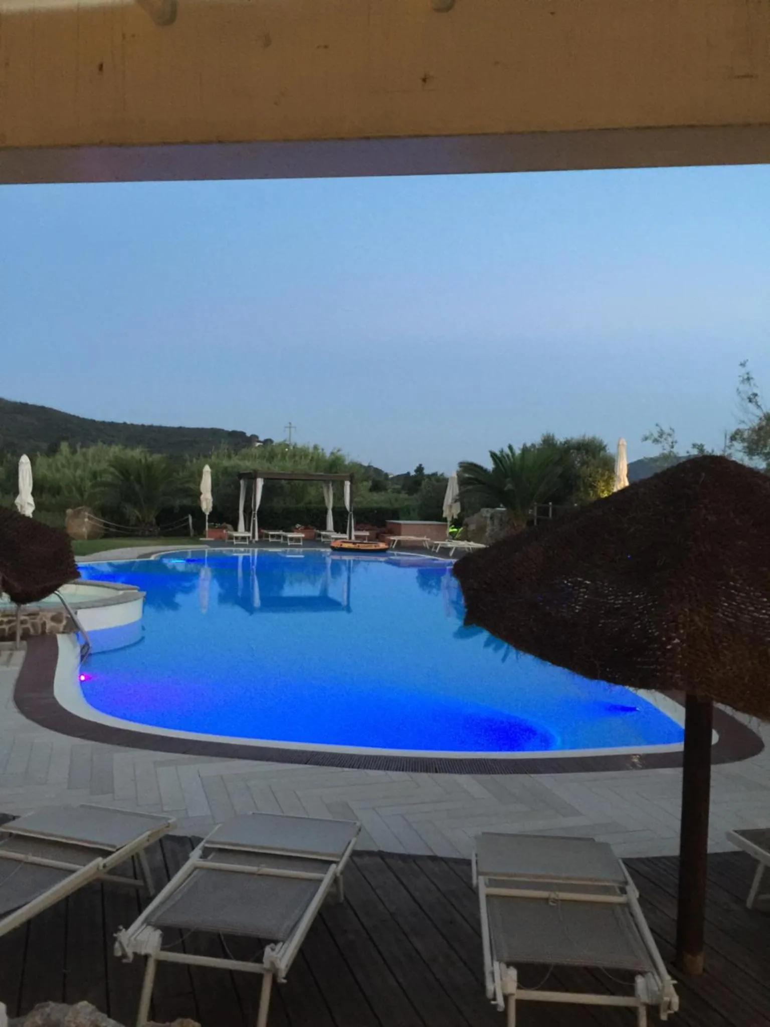 Une piscine illuminée avec des transats et une vue sur la mer au loin.