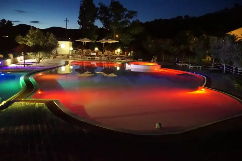 Piscine illuminée avec des lumières colorées et des transats.