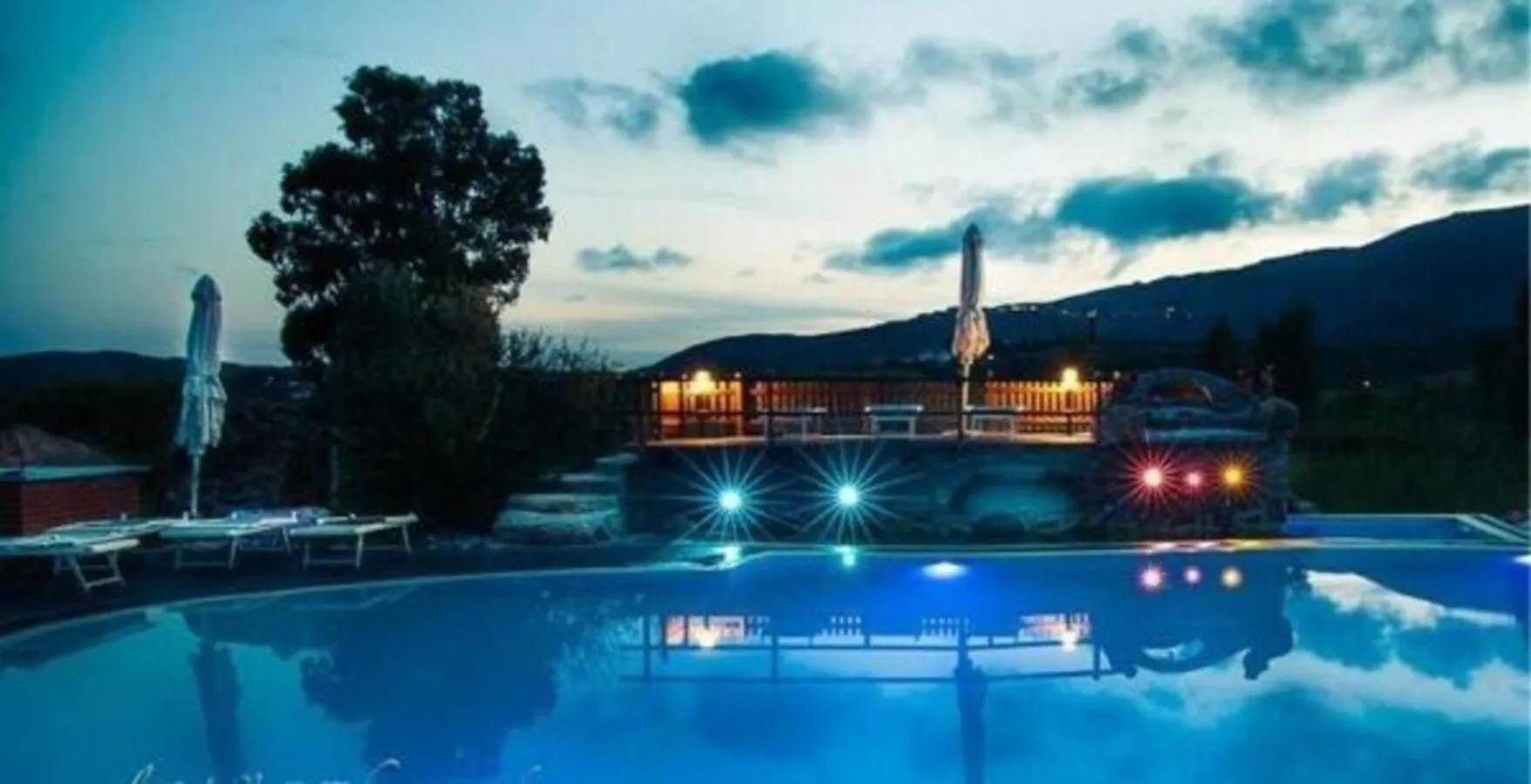 Piscine illuminée avec transats et végétation luxuriante au crépuscule.