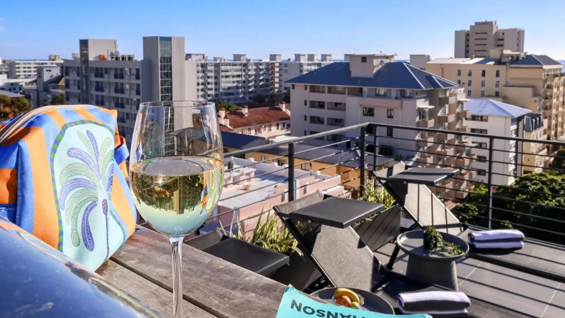 Un verre de vin et un coussin coloré sur une terrasse avec vue sur la ville.