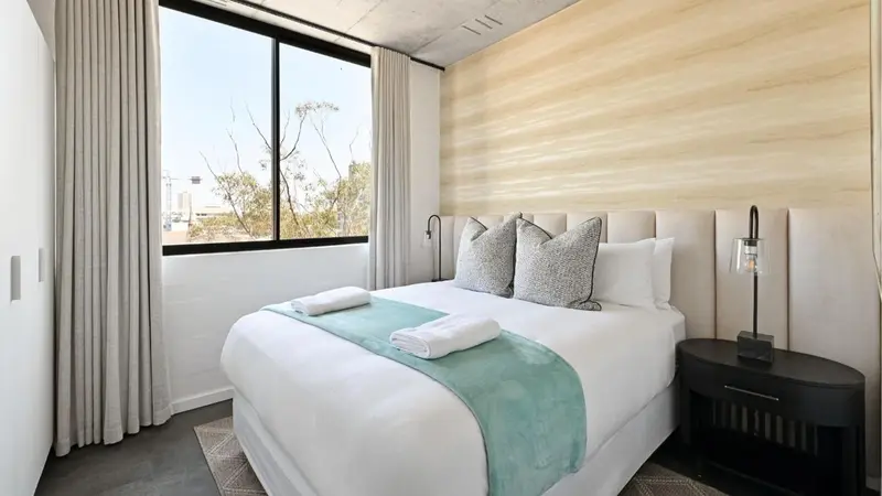 Une chambre lumineuse avec un grand lit recouvert d'oreillers et d'une couverture turquoise.