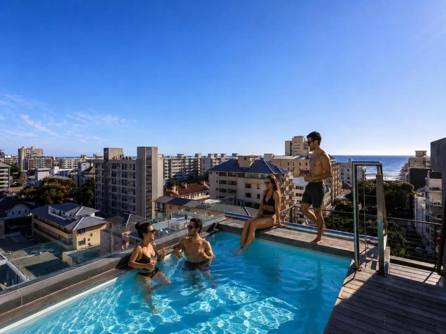 Des personnes se détendent au bord d'une piscine sur un toit avec vue sur la ville et la mer.