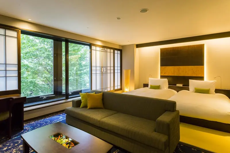 Une chambre lumineuse avec un canapé et deux lits simples face à une grande fenêtre.