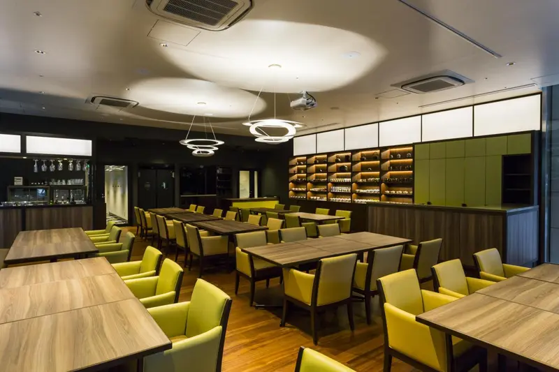Une salle lumineuse avec des tables et des chaises vertes et des étagères remplies de bouteilles.