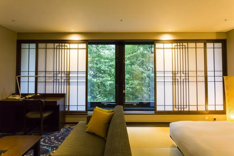 Une chambre lumineuse avec un canapé vert et une vue sur la végétation à travers des fenêtres japonaises.