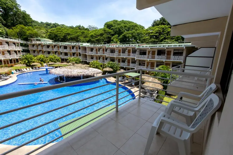 Vue sur une piscine et une végétation luxuriante depuis un balcon.