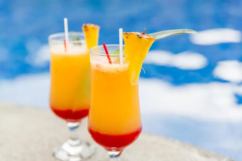 Deux cocktails colorés sont servis au bord d'une piscine.