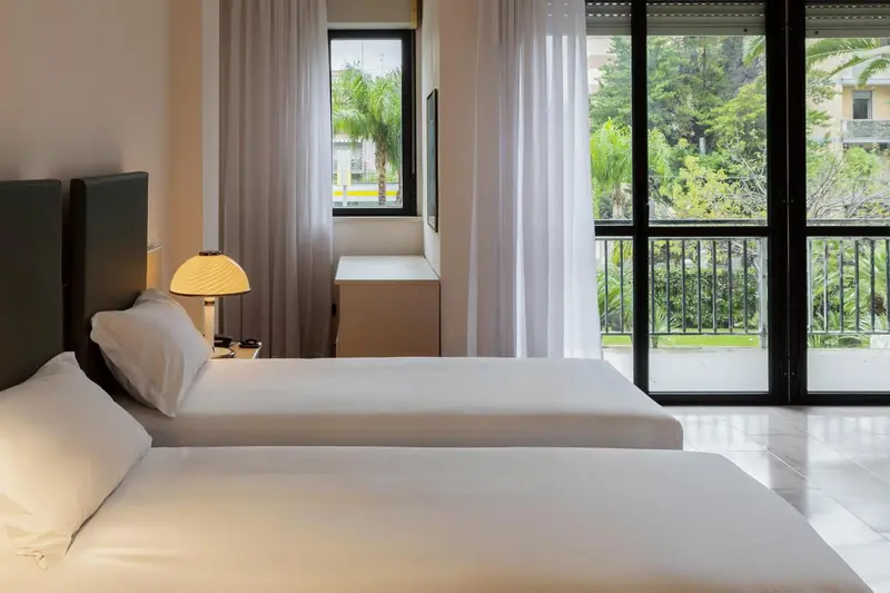 Une chambre lumineuse avec deux lits simples et un accès à un balcon.