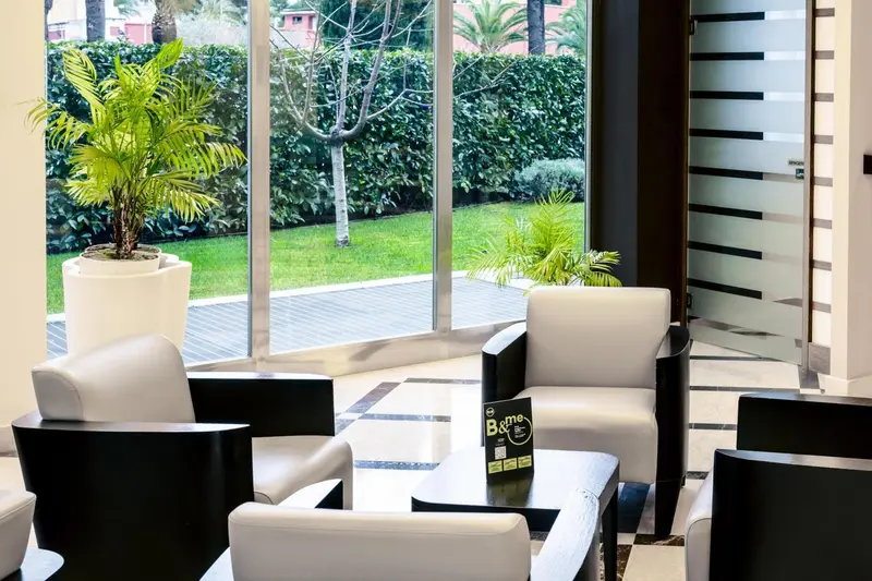 Un espace salon moderne avec des fauteuils blancs et noirs près d'une grande fenêtre donnant sur un jardin.