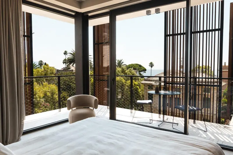 Une chambre lumineuse s'ouvre sur une terrasse avec vue sur la végétation et la mer.
