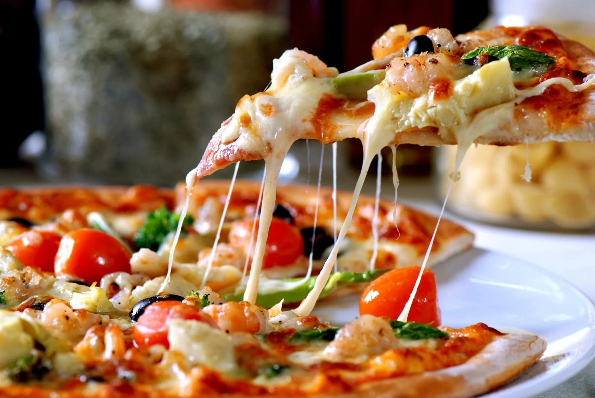 Une part de pizza dégouline de fromage fondu, avec des garnitures colorées.