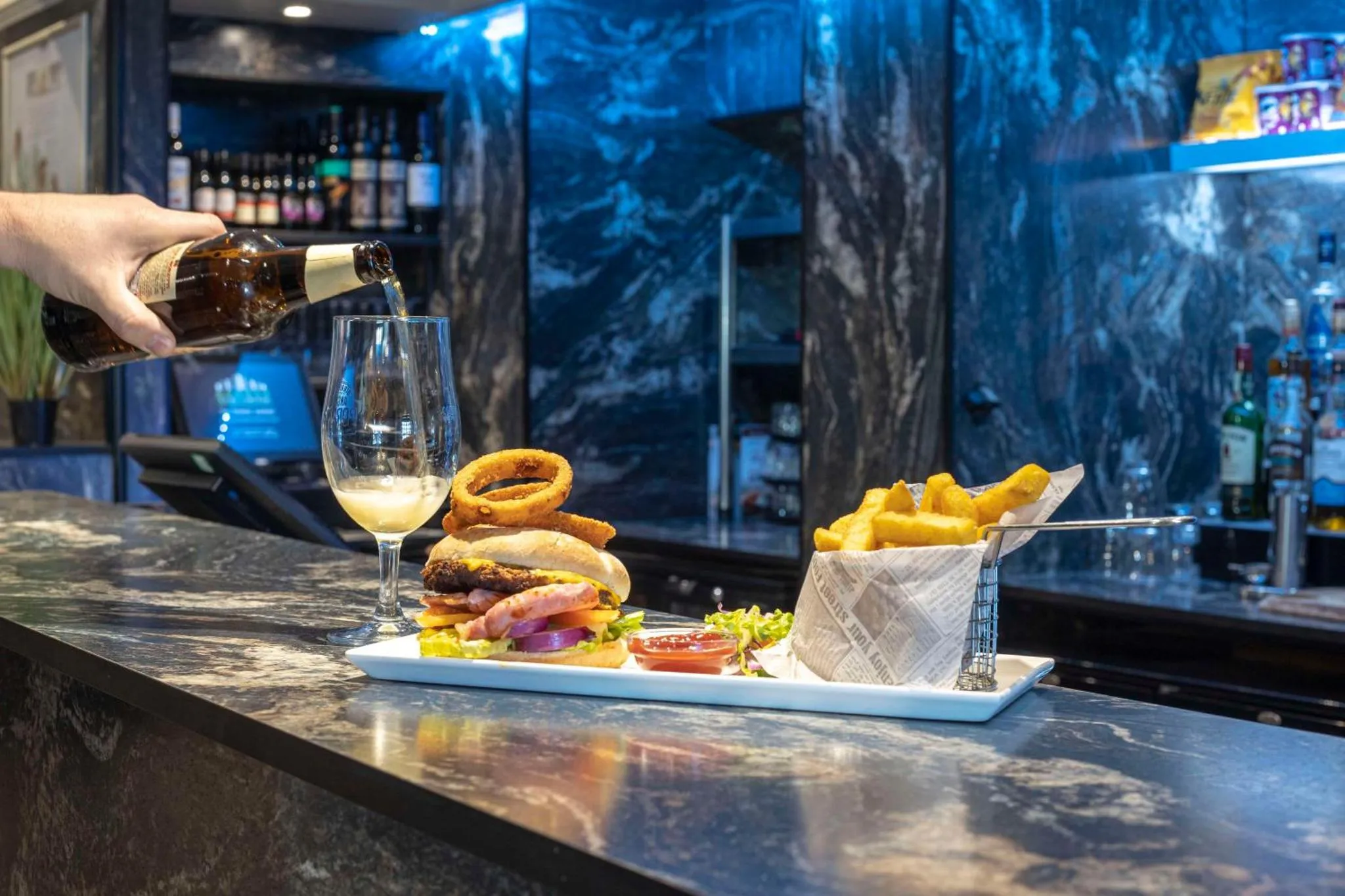 Un verre est rempli de bière devant un hamburger, des frites et des boissons sur un comptoir.