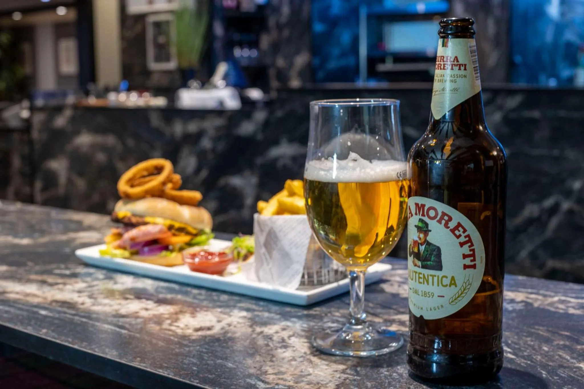 Un verre de bière et une assiette de nourriture sont posés sur un comptoir sombre.