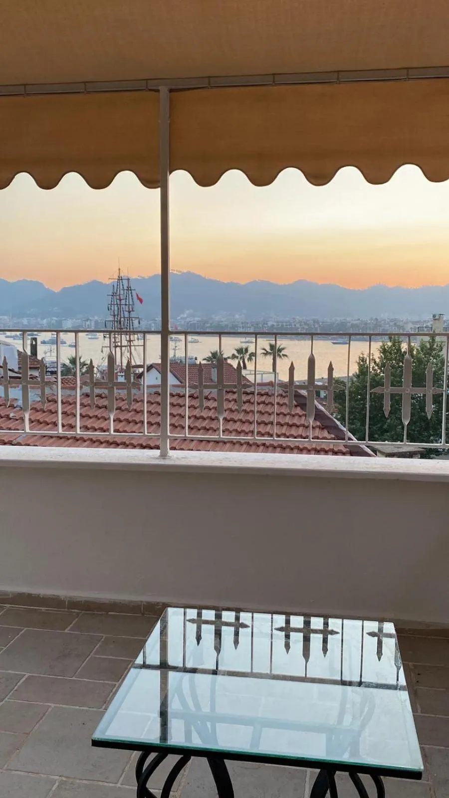 Une terrasse avec une table basse offre une vue sur la mer et les montagnes au coucher du soleil.