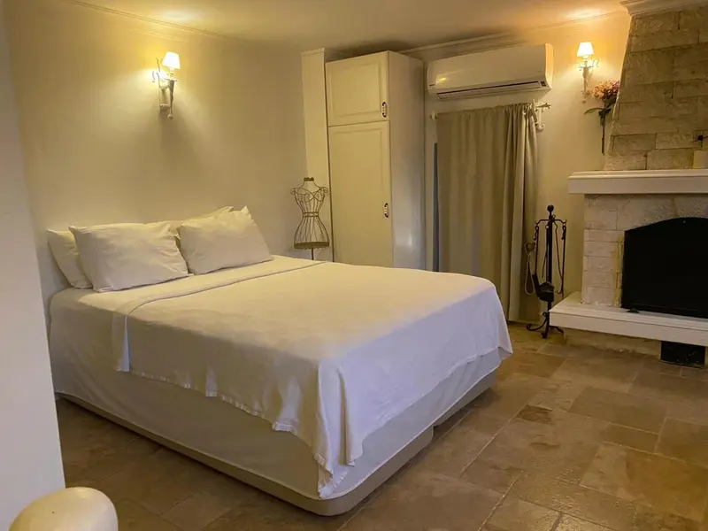 Une chambre lumineuse avec un lit blanc et une cheminée en pierre.
