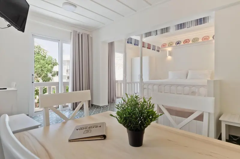 Une table blanche et des chaises se trouvent devant un lit superposé dans une pièce lumineuse.