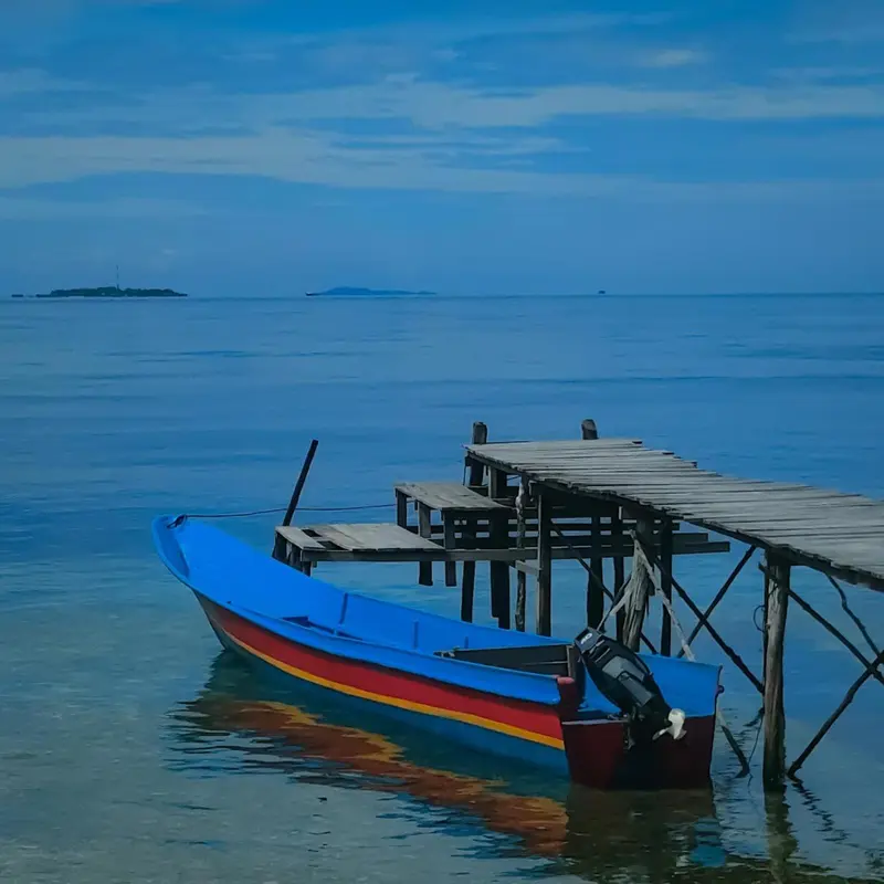 Un bateau coloré est amarré à une jetée en bois sur une mer calme.