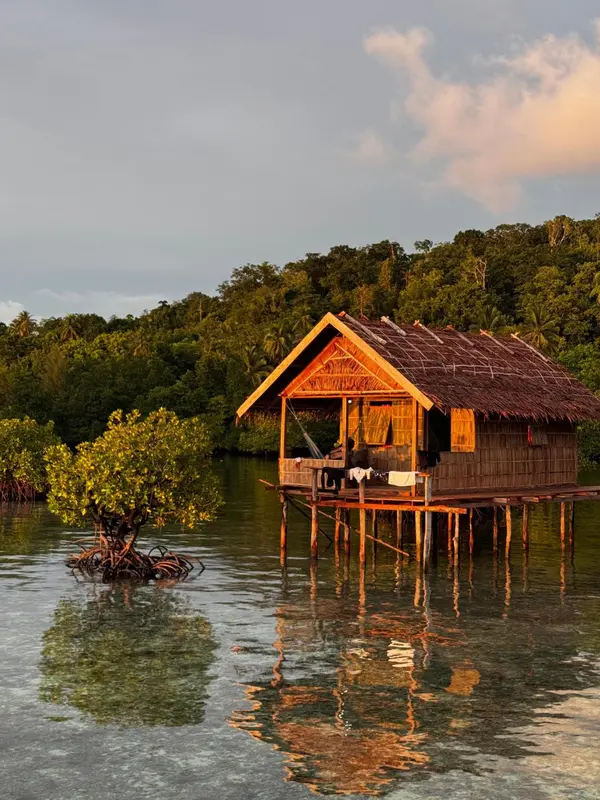 Une cabane en bois sur pilotis se reflète dans l'eau calme.