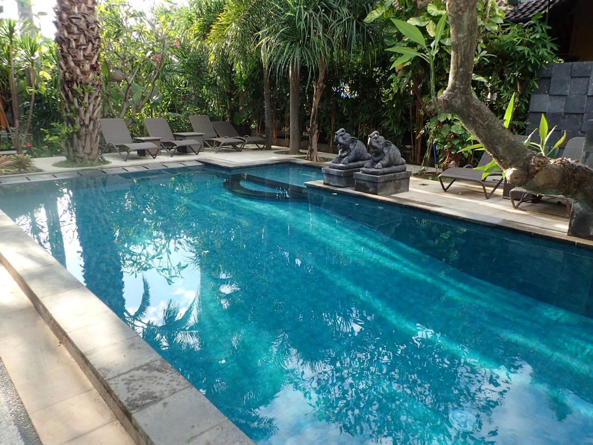 Une piscine rectangulaire bordée d'une terrasse avec des chaises longues et des statues.