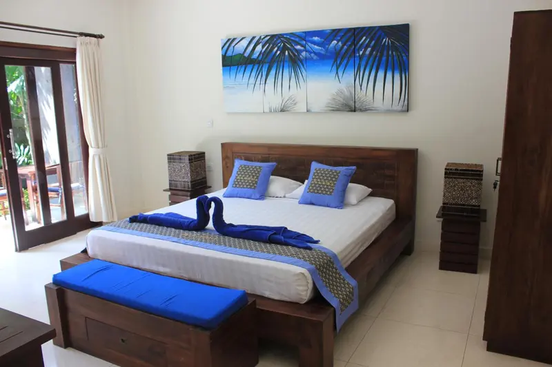Une chambre lumineuse avec un grand lit recouvert d'une courtepointe bleue et de coussins assortis.
