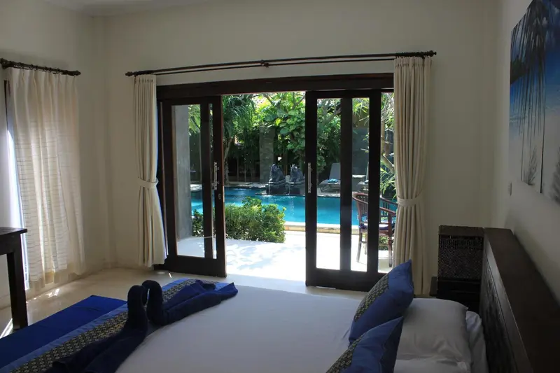 Une chambre lumineuse s'ouvre sur une piscine par de grandes baies vitrées.
