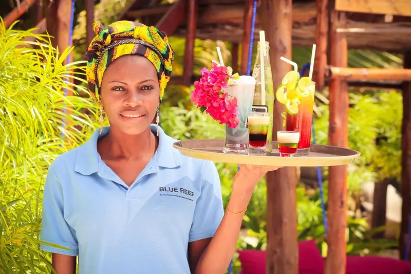 Une serveuse souriante porte un plateau de boissons colorées.