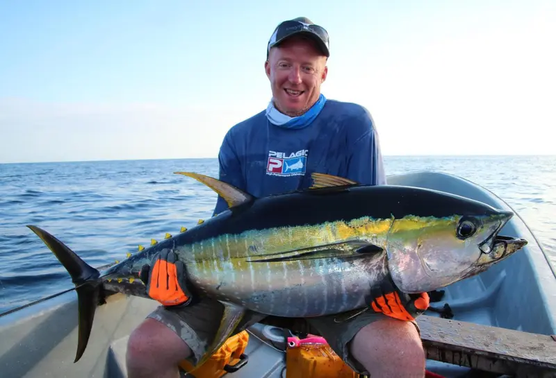 Un homme souriant tient un gros poisson bleu et jaune sur un bateau.