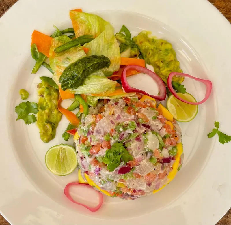 Assiette colorée de ceviche garnie de légumes frais et d'une sauce crémeuse.