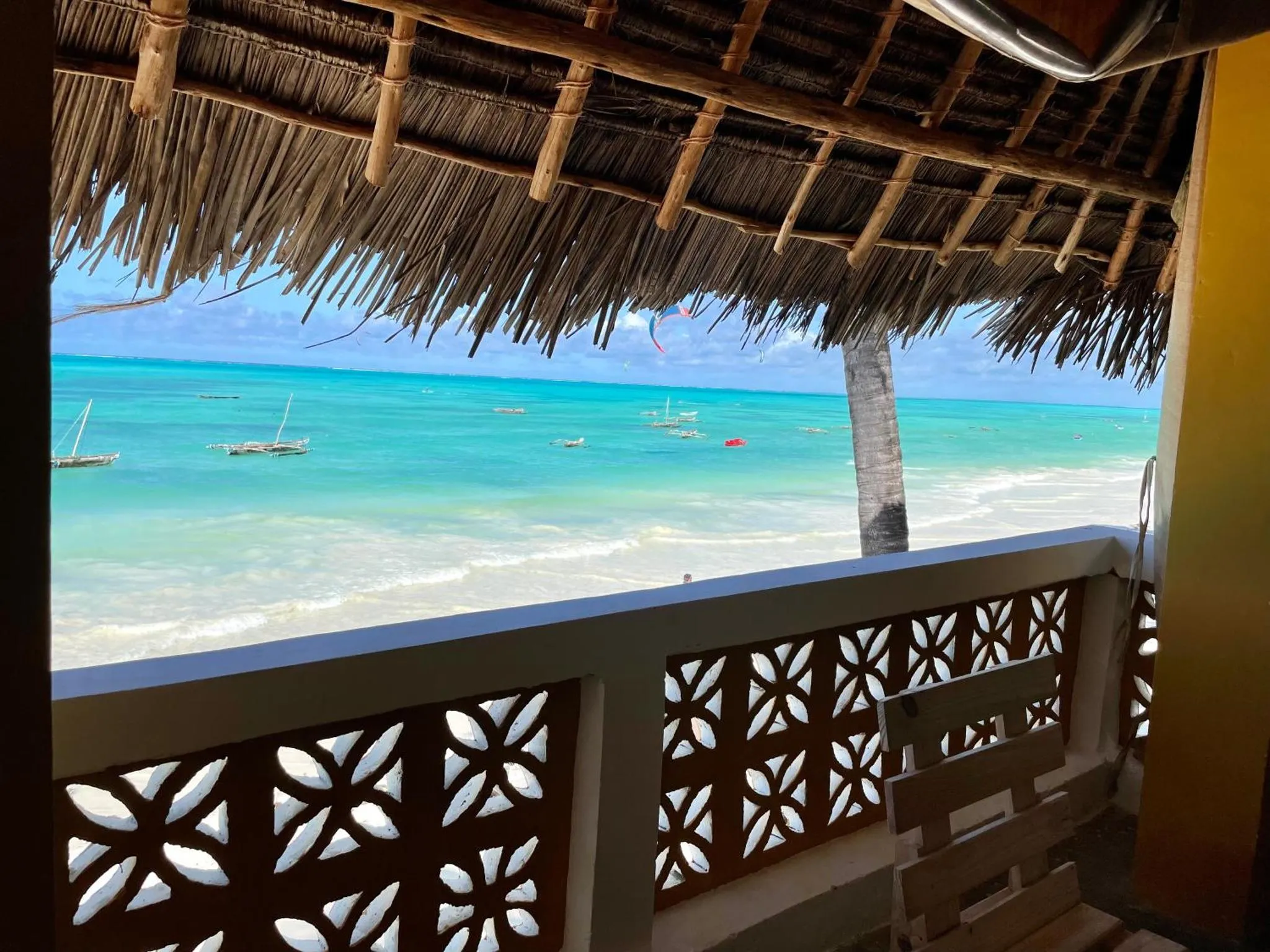 Vue sur une plage de sable blanc et une mer turquoise depuis une terrasse ombragée.