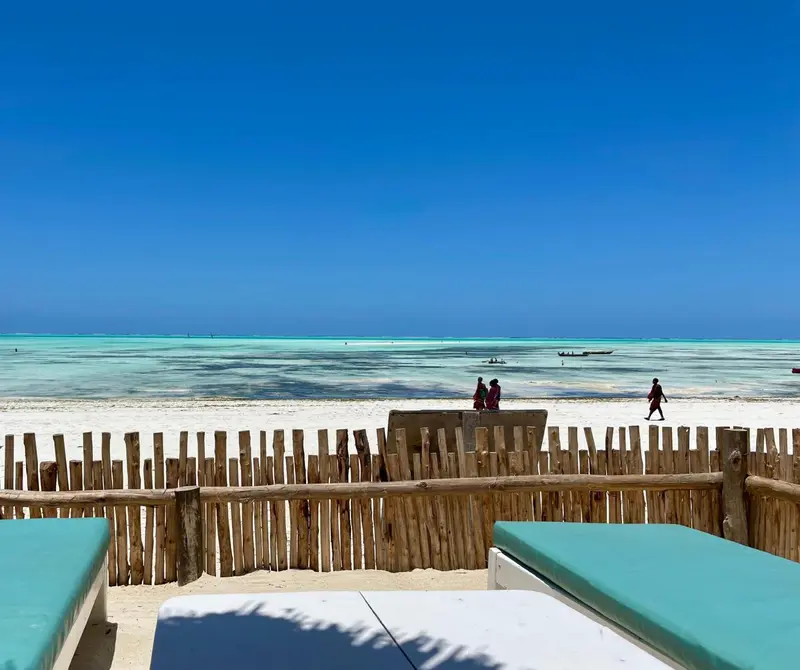 Plage de sable blanc bordée d'une eau turquoise sous un ciel bleu dégagé.