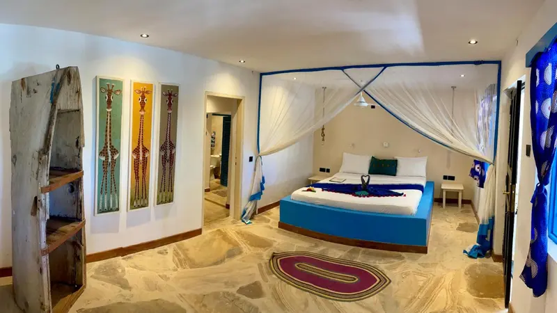 Une chambre lumineuse avec un grand lit recouvert de tissus bleus et verts.