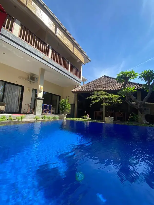 Une piscine rectangulaire bleu clair est au premier plan, avec un bâtiment jaune et blanc en arrière-plan.