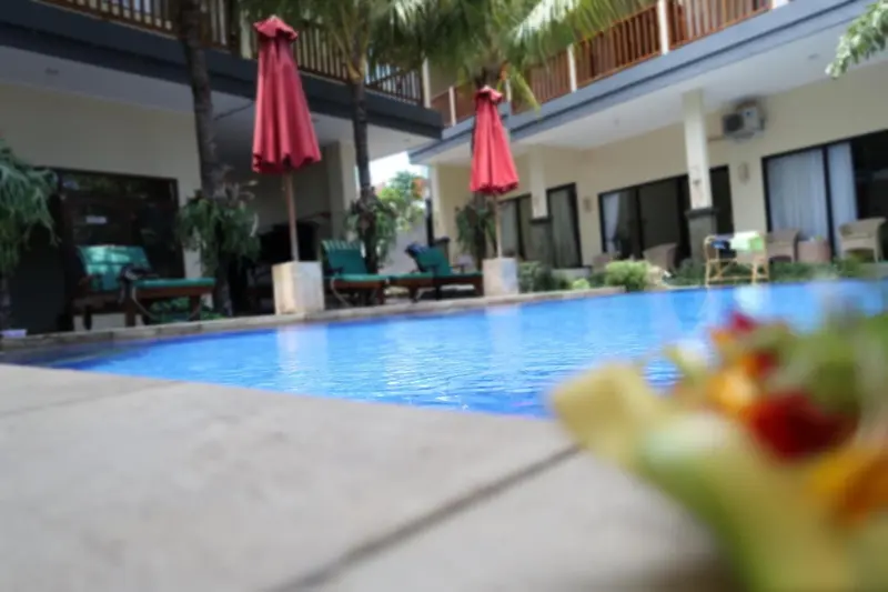 Une piscine turquoise au premier plan, entourée de chaises longues et de végétation tropicale.