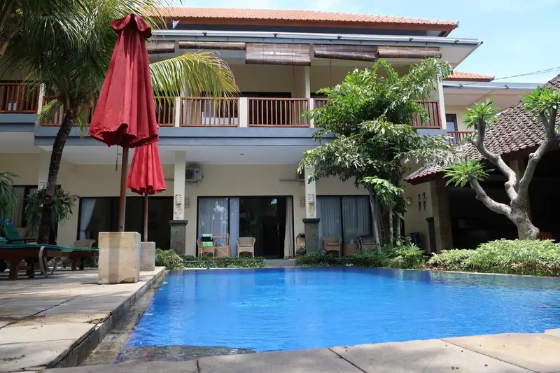 Façade d'un bâtiment avec une piscine au premier plan et des transats.