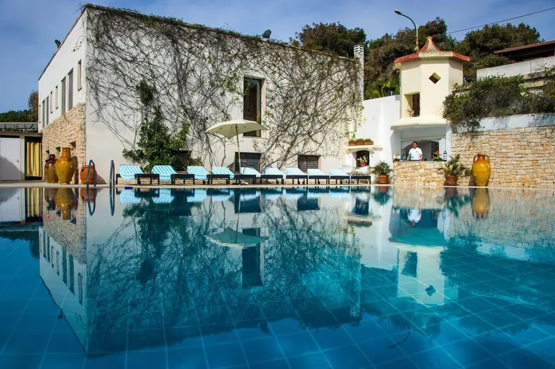 Piscine bleue reflétant un bâtiment blanc et un ciel bleu.