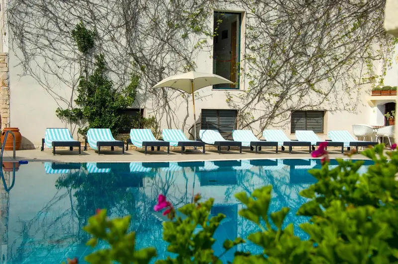 Transats bleus alignés au bord d'une piscine turquoise ombragée par des parasols.