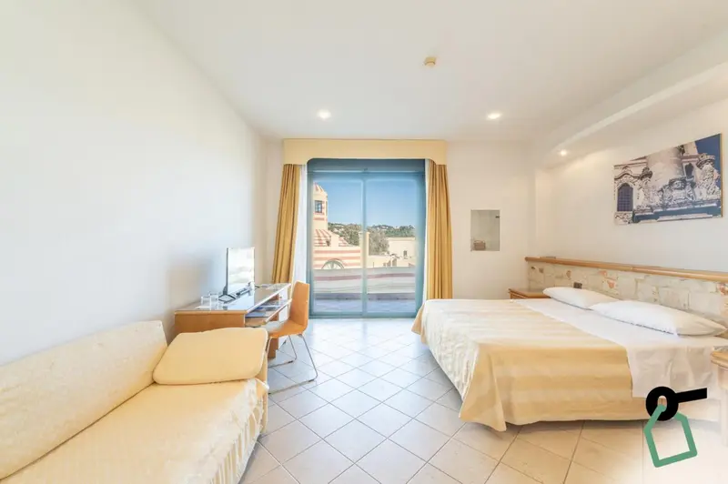 Chambre lumineuse avec canapé, bureau et lit donnant sur une terrasse.