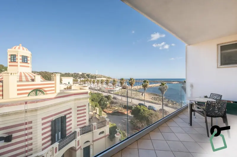 Vue d'une terrasse avec une rambarde vitrée donnant sur la mer et un paysage urbain.