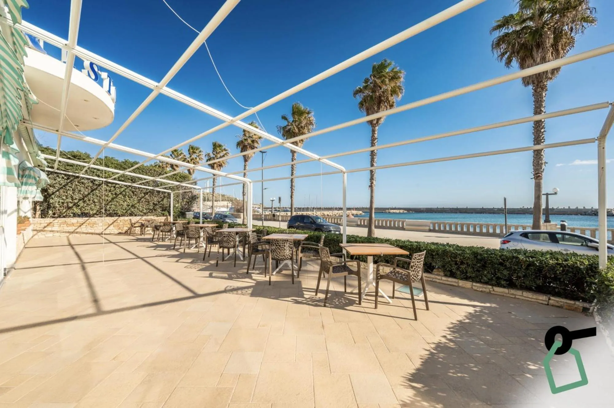 Terrasse ombragée avec tables et chaises en bord de mer.