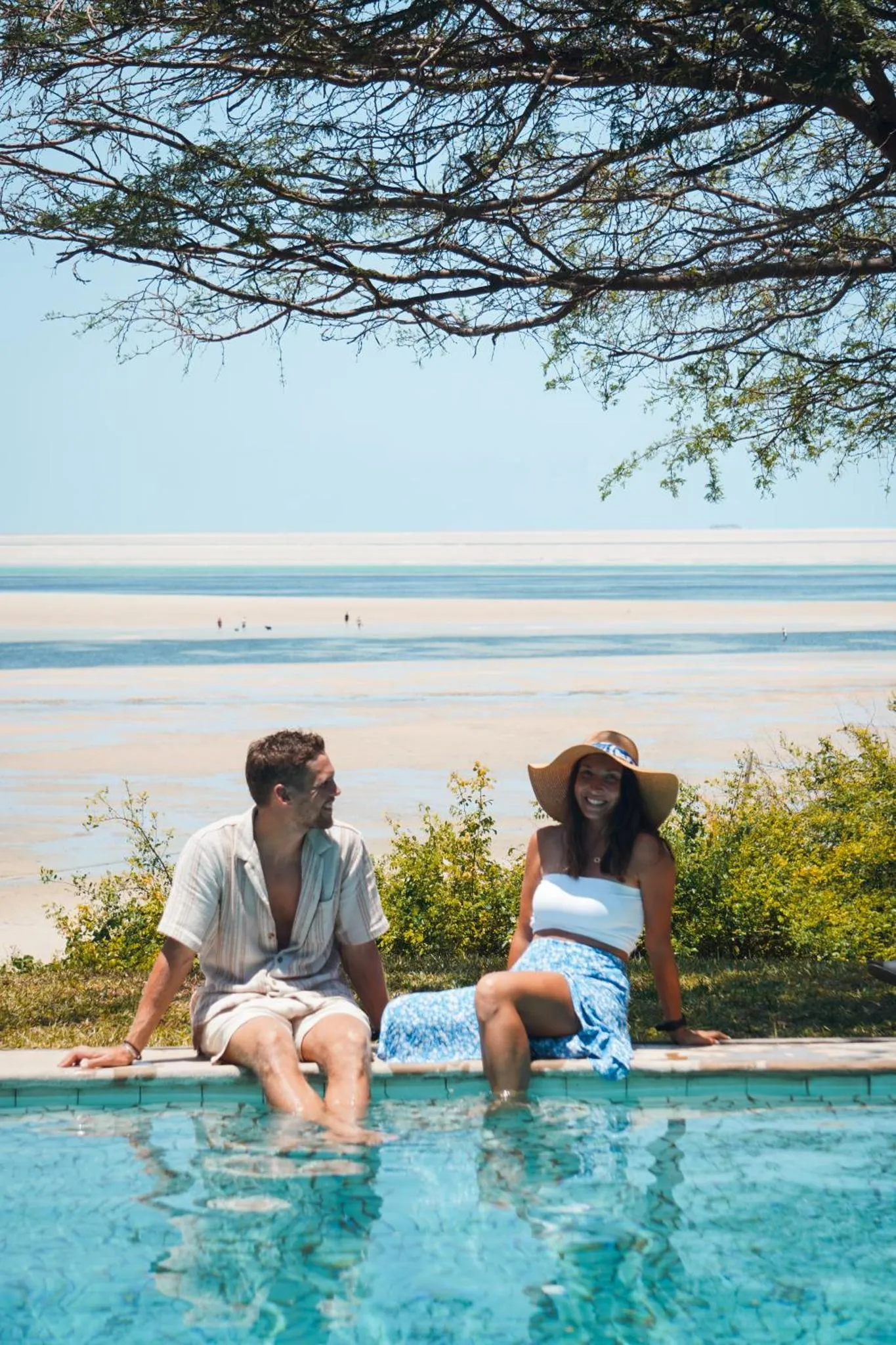 Un couple souriant est assis au bord d'une piscine avec vue sur la mer.