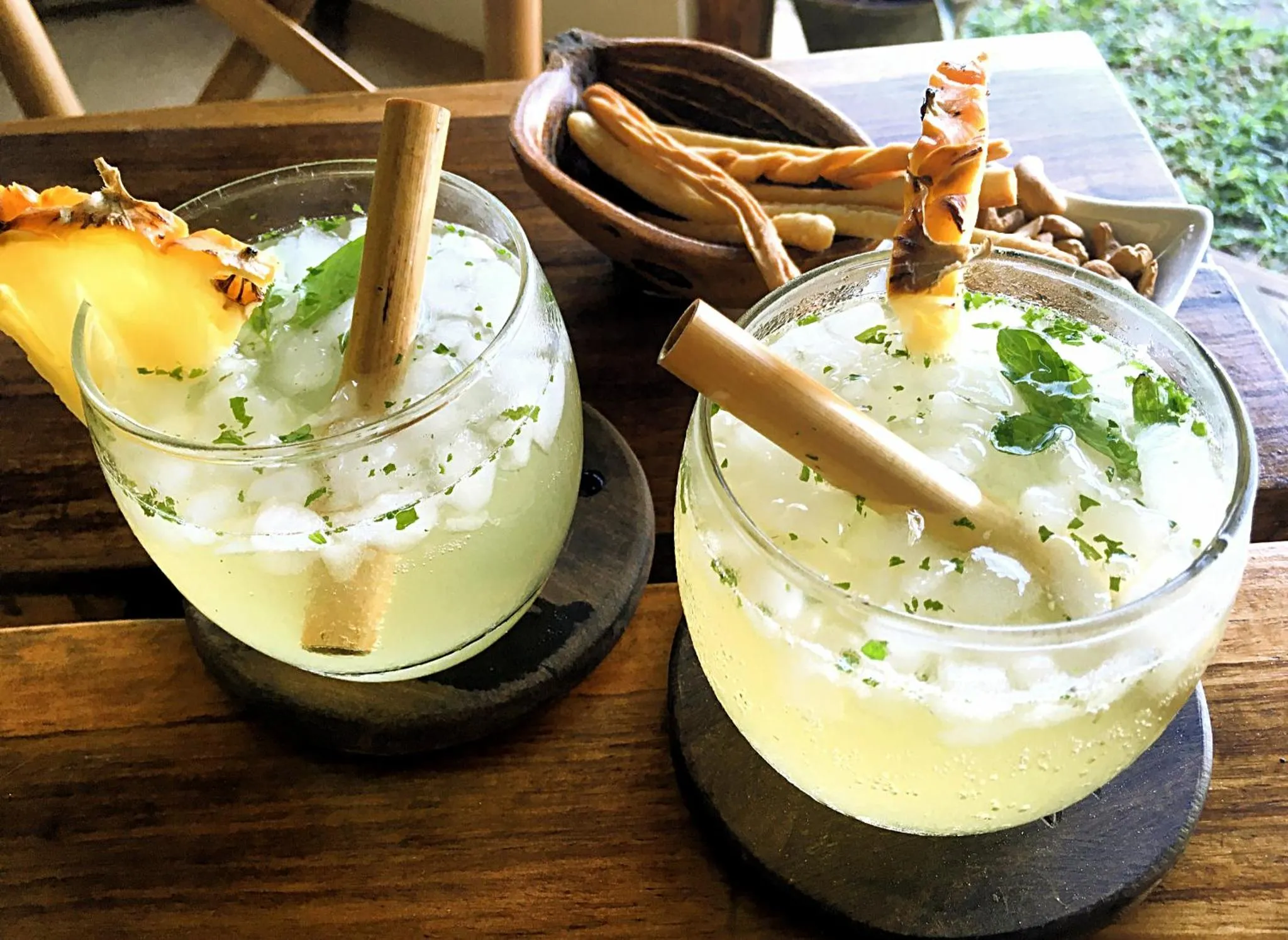 Deux cocktails exotiques garnis de fruits frais et de bâtons de cannelle sont servis sur une table en bois.