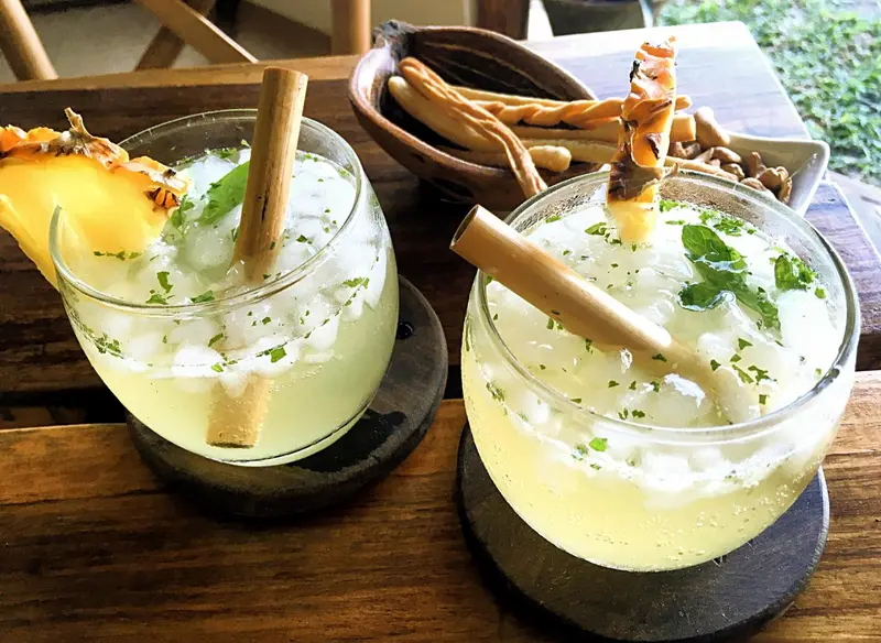 Deux cocktails exotiques garnis de fruits frais et de bâtons de cannelle sont servis sur une table en bois.