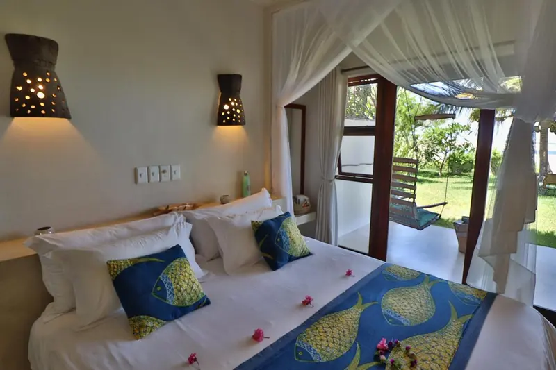 Une chambre lumineuse avec un lit décoré de coussins colorés et une vue sur une végétation luxuriante.