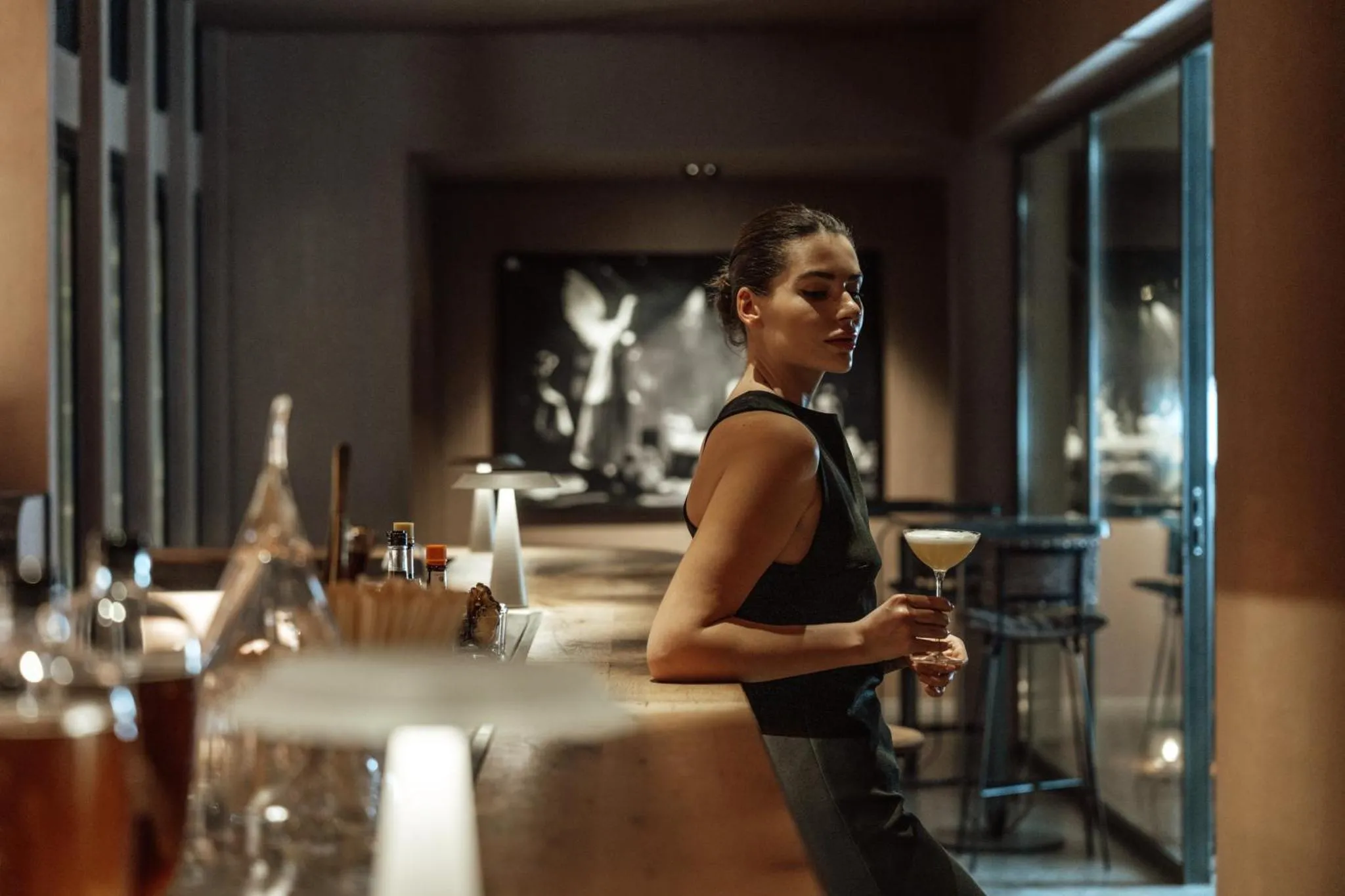 Une femme élégante tient un verre au comptoir d'un bar.