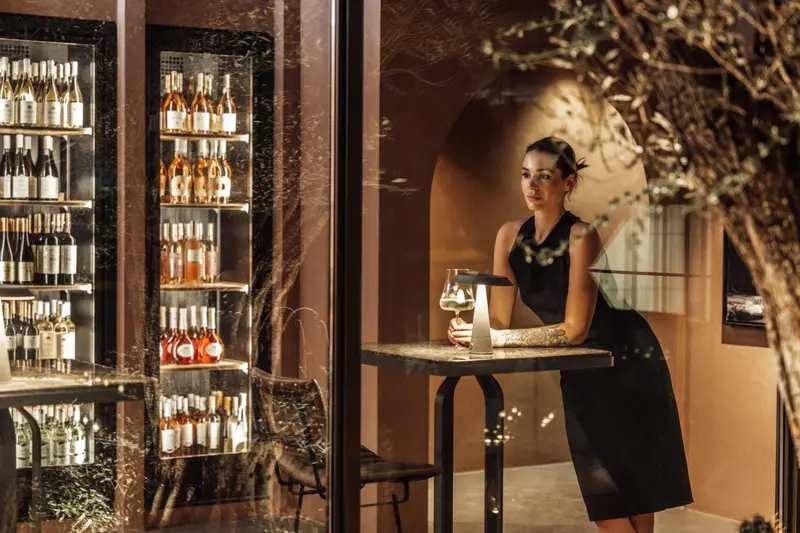 Une employée se tient près d'une table avec une bouteille et des verres dans un espace élégant.
