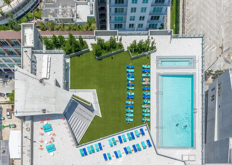 Vue aérienne d'une piscine rectangulaire entourée d'une pelouse artificielle et de chaises longues bleues.